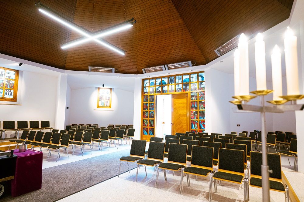 Innenraum der Aufbahrungshalle mit Stuhlreihen, Kerzenleuchtern und hellem Holzdach