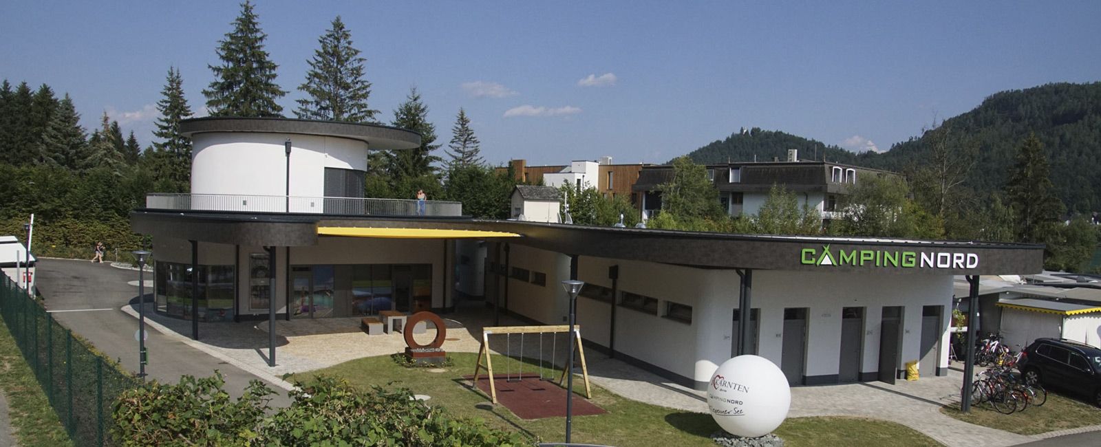 Empfangsgebäude des Campingplatzes Nord mit Spielplatz und Bäumen
