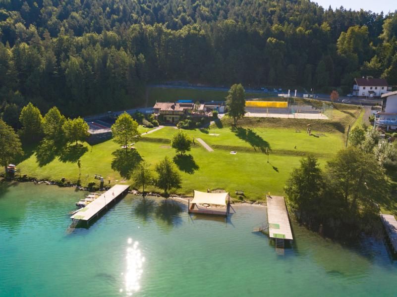 Luftaufnahme des Sportstrandbads Süd mit Liegewiese, Stegen und Beachvolleyballplätzen am Waldrand