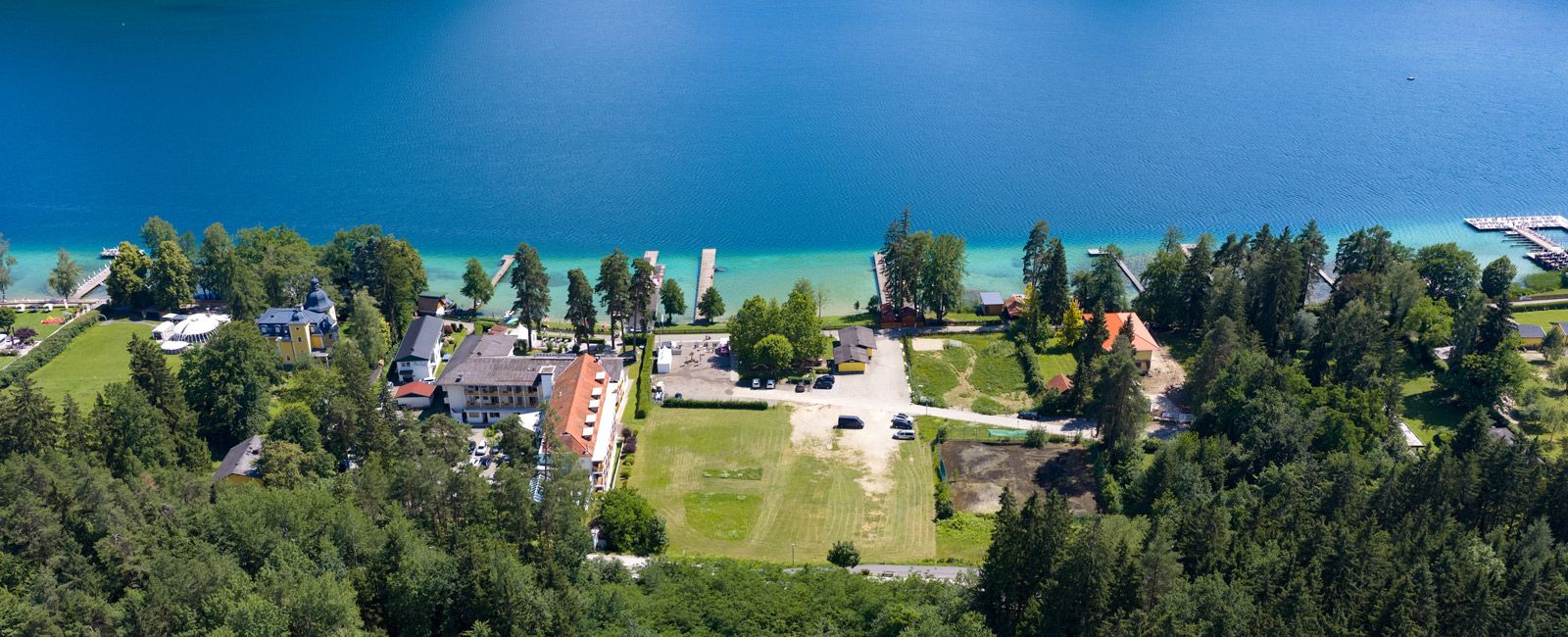 Luftaufnahme der Norduferpromenade mit Wiese, Bäumen und dem Klopeiner See im Hintergrund