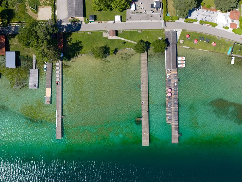 Luftaufnahme von oben: lange Holzstege führen von der Liegewiese in den Klopeiner See